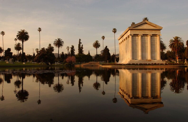 A large white mausoleum sits on the edges of a lake with palm trees in the background.