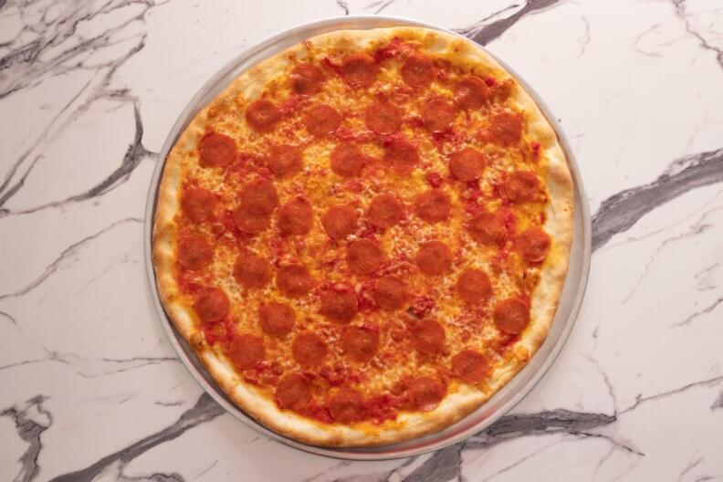 A pepperoni pizza sits on a marble countertop.