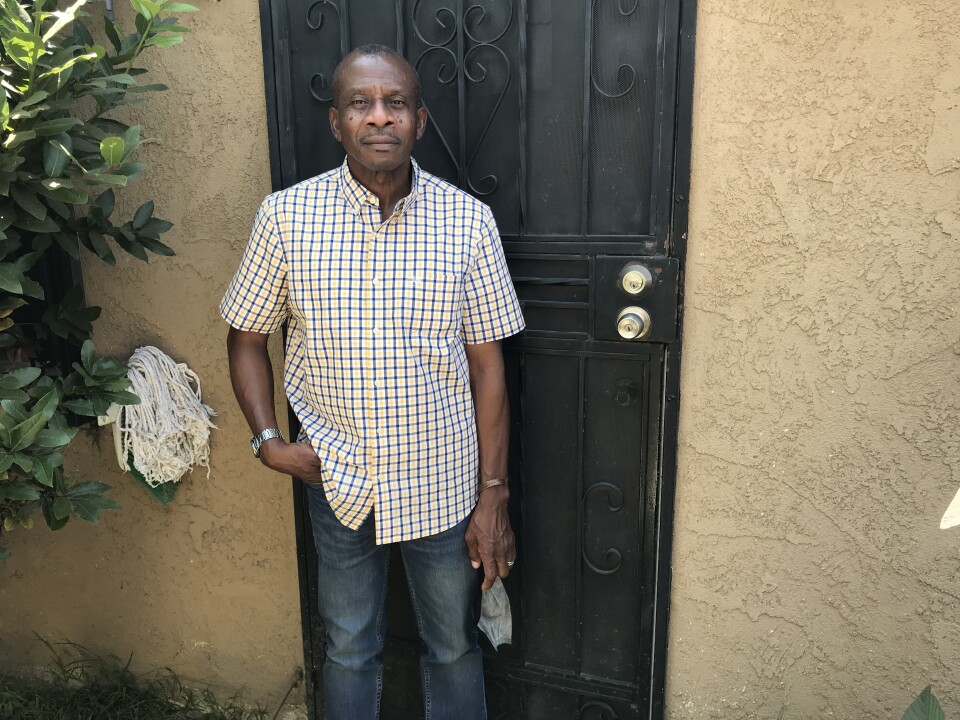 A man stands in front of the door to his apartment.
