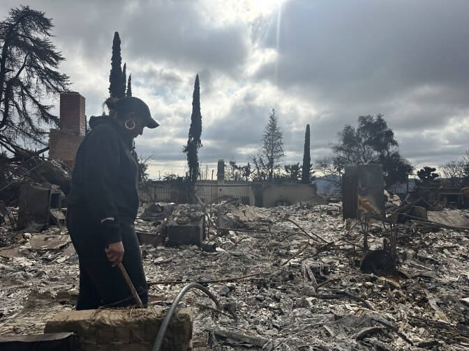 A woman stands atop the rubble of a home.