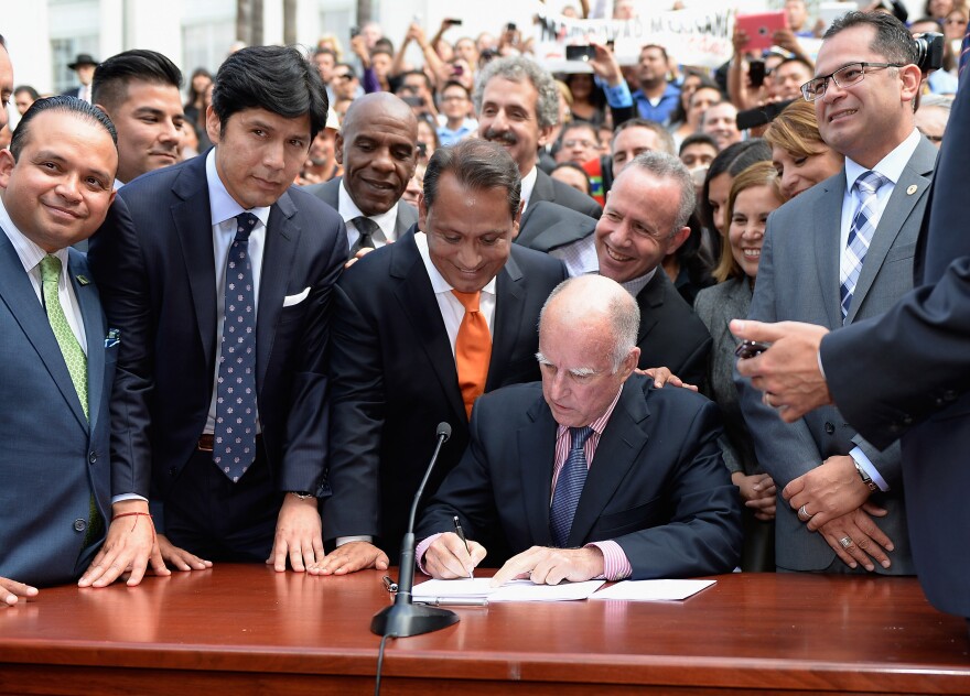 California Governor Jerry Brown (C) signs bill AB60 as Democratic State Senator Kevin de Leon (2nd L), state assemblyman Luis Alejo (L) and councilman Gil Cedillo (3rd L) watch on the steps of Los Angeles City Hall  October 3, 2013 in Los Angeles, California. California Assembly Bill 60 also known as the Safe and Responsible Driver Act allows illegal immigrants to receive a permit to legally drive in California.  