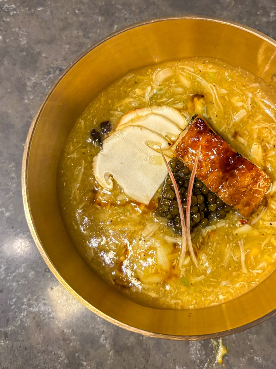 Golden bowl containing Dungeness crab soup with fresh noodles, pine mushrooms, and a quenelle of what appears to be tofu or cream, garnished with caviar.