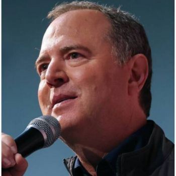 An older man with short dark hair is wearing a dark shirt. He is holding a microphone and speaking to someone off camera.