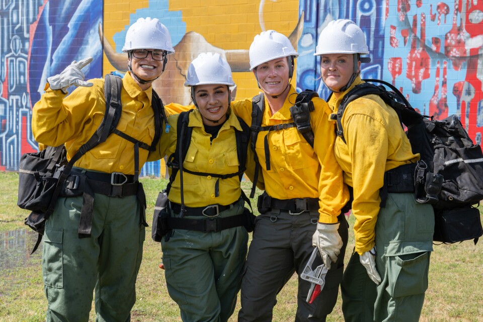 Four women pose wearing firefighting gear.