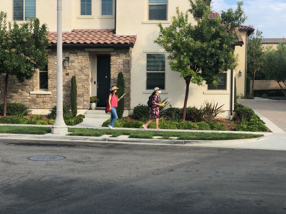 Two women of Asian descent wearing hats canvass a neighborhood in Orange County. 