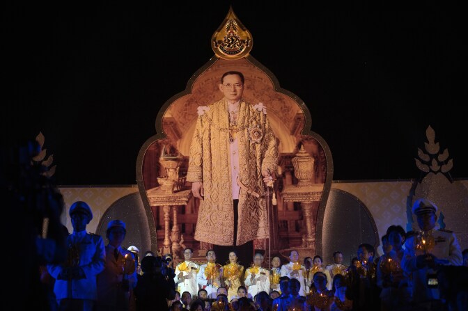 Thai Prime Minister Prayut Chan-O-Cha (centre L) holds a candle and sing songs in front of a giant portrait of King Bhumibol Adulyadej (top) as he and other offcials gather in front of the Grand palace, on the occasion of his 87th birthday in Bangkok on December 5, 2014. Thailand's ailing King Bhumibol Adulyadej cancelled plans to hold a public annual audience marking his 87th birthday on December 5, heightening anxiety in the deeply divided kingdom over the adored leader's health. AFP PHOTO/ Nicolas ASFOURI        (Photo credit should read NICOLAS ASFOURI/AFP/Getty Images)