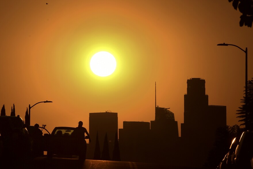 A silhouette of buildings, lampposts, a person running and a car underneath a blazing hot sun.