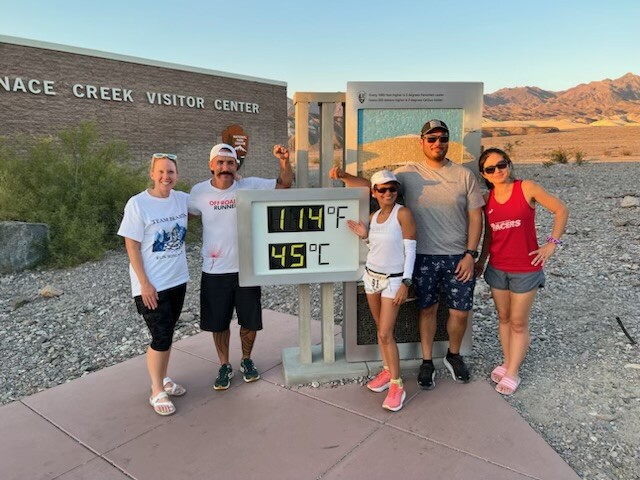 A group of people in summer clothes pose next to a thermometer with a reading of "114 degrees F" and "45 degrees C"