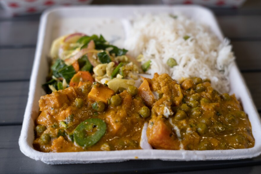 A styrofoam takeout container holds a serving of Indian food with white rice.