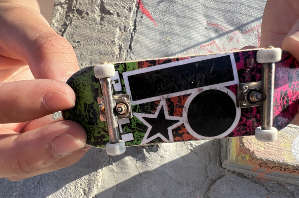 Levi Hernandez shows off a typical fingerboard. It has white wheels, metal frames and a decorated bottom deck.