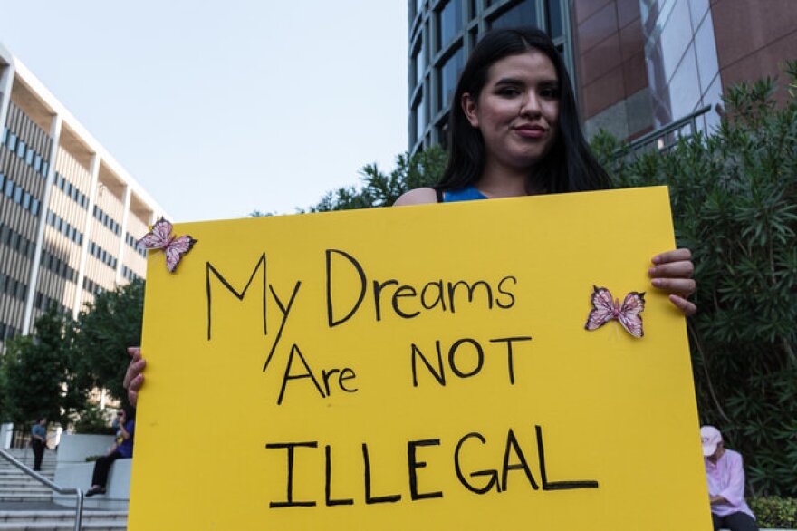 A young woman holds up a yellow sign, decorated with two butterflies, that reads, "my dreams are not illegal."