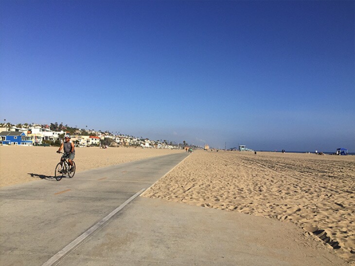 A cyclist takes off along a bike path that carves its way through the sand, with a few of the ocean waves on one side, and beach-ront real estate on the other.