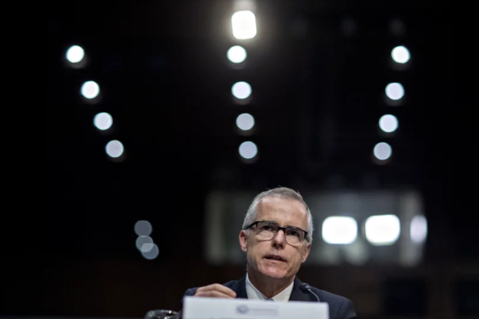  A man with black framed glasses and light skin is wearing a jacket and speaking into a microphone.