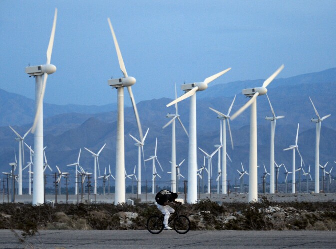 A man rids his bike against the win as giant wind turbines are powered by strong winds at sunset on March 27, 2013 in Palm Springs, California. According to reports, California continues to lead the nation in green technology and has the lowest greenhouse gas emissions per capita, even with a growing economy and population. 