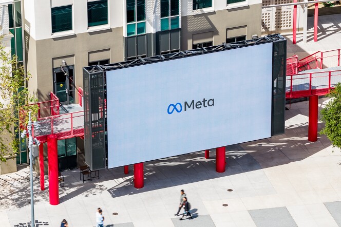 A large white screen in front of a beige and white building with many windows. On the screen is the word "Meta"