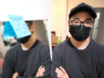 Ed Park, in a black t-shirt, with a black mask, black glasses and black cap looks at the camera while standing next to a mirror that has a blue post-it note stuck to it.