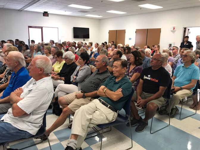 Dozens of people sit in chairs during the meeting.