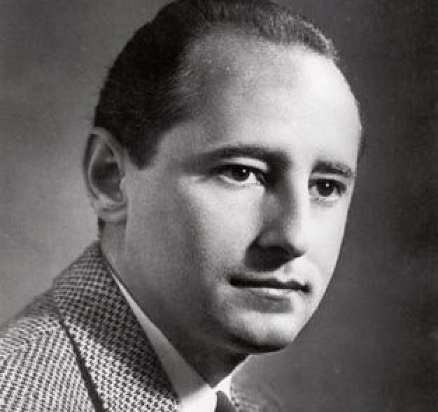 A man with light-tone skin and a receding hairline is photographed in a tweed suit jacket