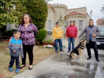 A family of five stand in front of their home, along with their pet German Shepherd