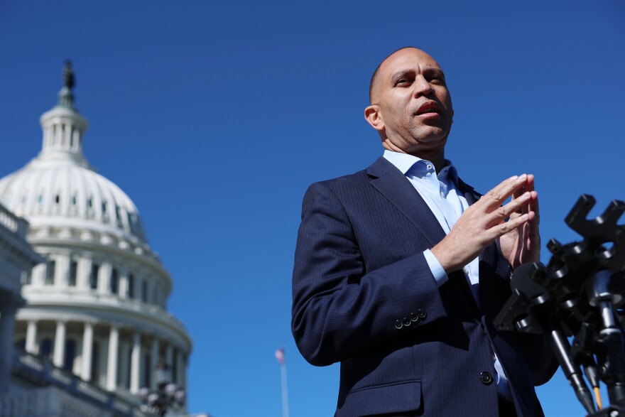 A Black man in a suit with no tie stands in front of the Capitol.