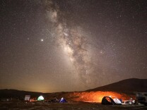 Bright objects in the night sky appear in a very starry sky over a campsite. 