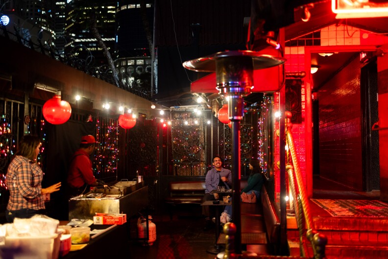 An outdoor bar patio at night with metal gated walls full of Christmas lights and hanging red lanterns.