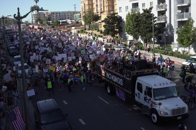 A crowd of people march behind a large truck.