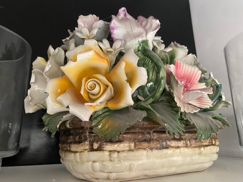 A ceramic vase that looks like a window box of flowers, with a basket, yellow, purple, and red flowers over green leaves.