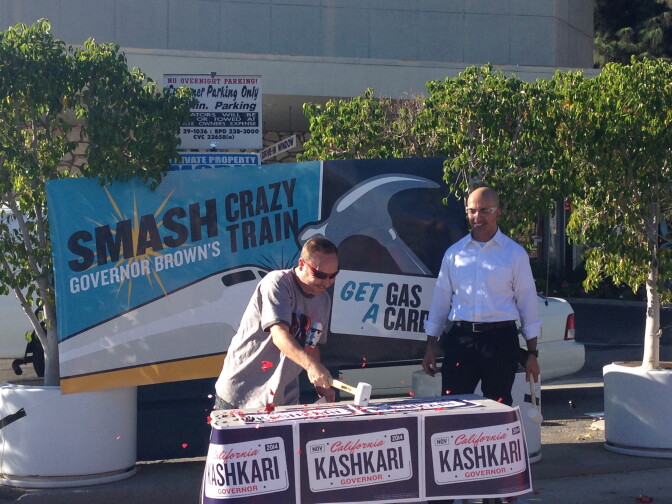 Republican Neel Kashkari looks on as a supporter breaks apart a plastic toy train in exchange for a $25 gas card. 