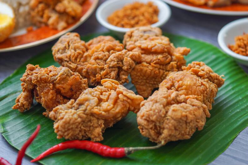 battered, fried chicken pieces on a green mat next to a couple red chili peppers