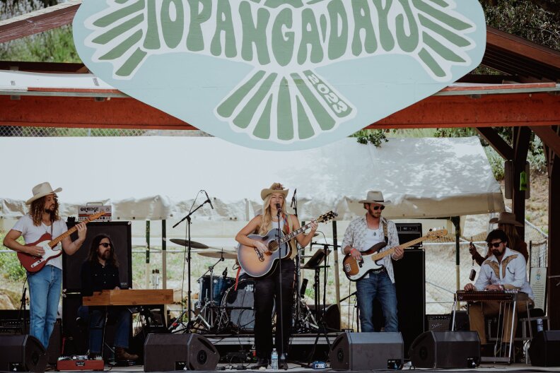 A band plays on an outdoor stage during the daytime while a "Topanga Days 2023" sign hangs above them.