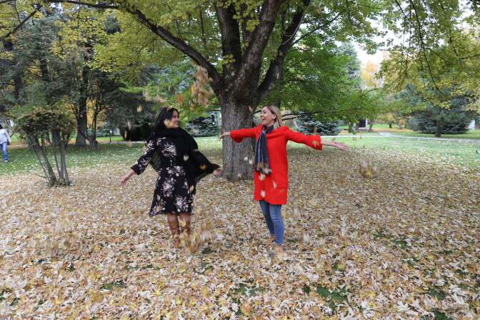 Women enjoy the leaves dropped from a tree displaying autumn colors in Ankara, Turkey on October 25, 2017.