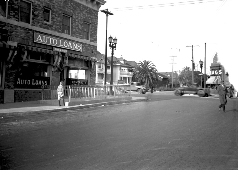 A 1927 photo shows a brick building with an Auto Loans sign. Underneath a boy walks down the stairs of a pedestrian tunnel as cars use the street in the background.