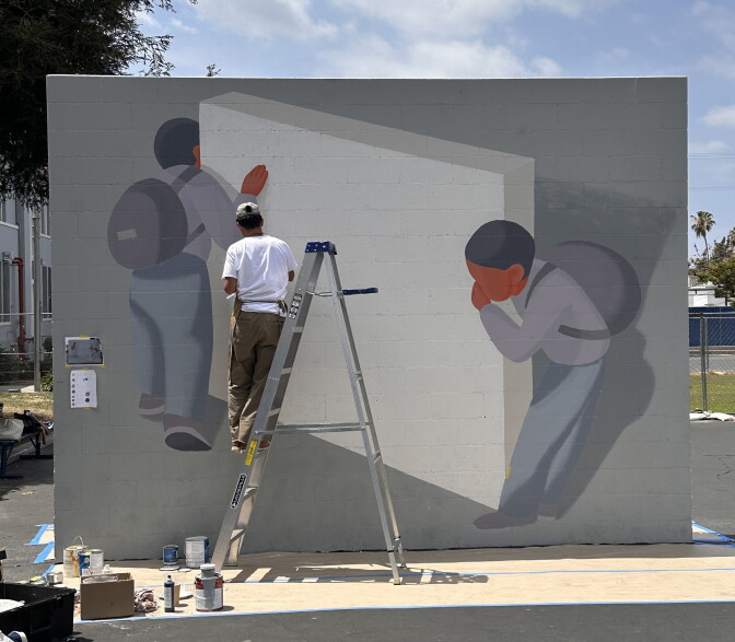 Mural on brick wall depicting two people looking around a handball court wall.