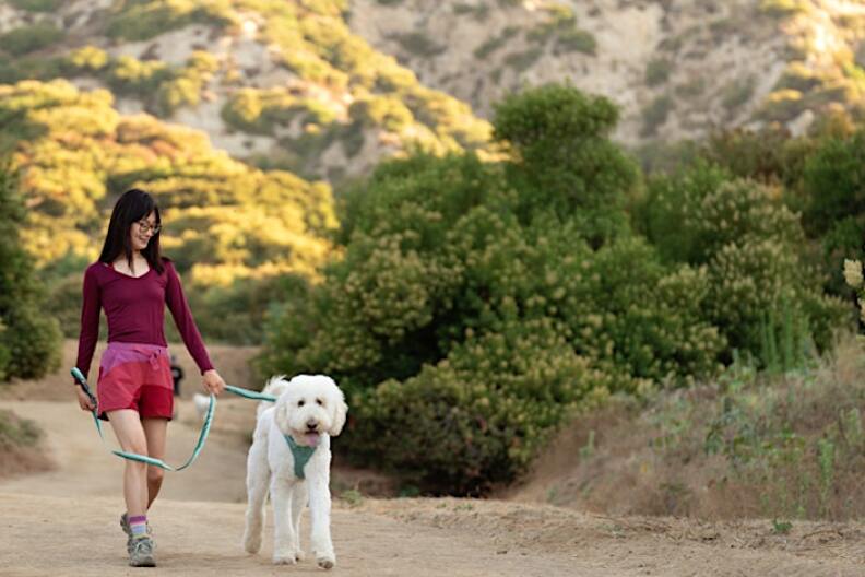 Image is a women smiling and hiking with her dog on top of a hill.