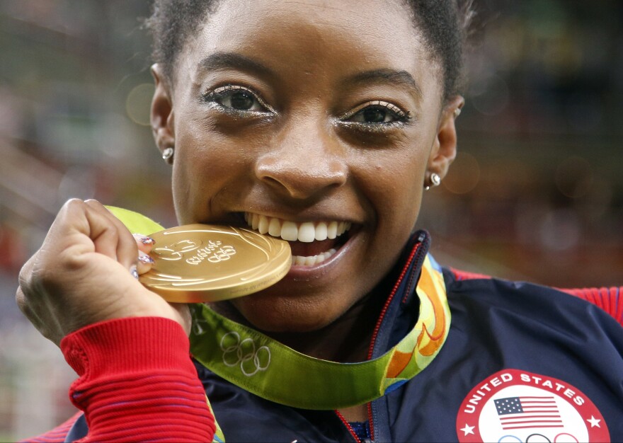 United States' Simone Biles bites her gold medal for the artistic gymnastics women's individual all-around final at the 2016 Summer Olympics in Rio de Janeiro, Brazil, Thursday, Aug. 11, 2016
