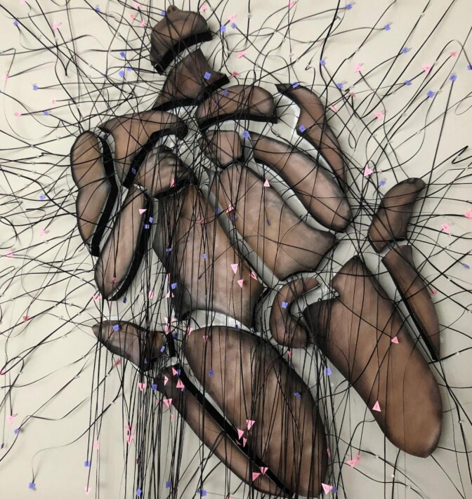 an art work features brown pieces arrange to for ma human body with strings and tiny flags running all over it