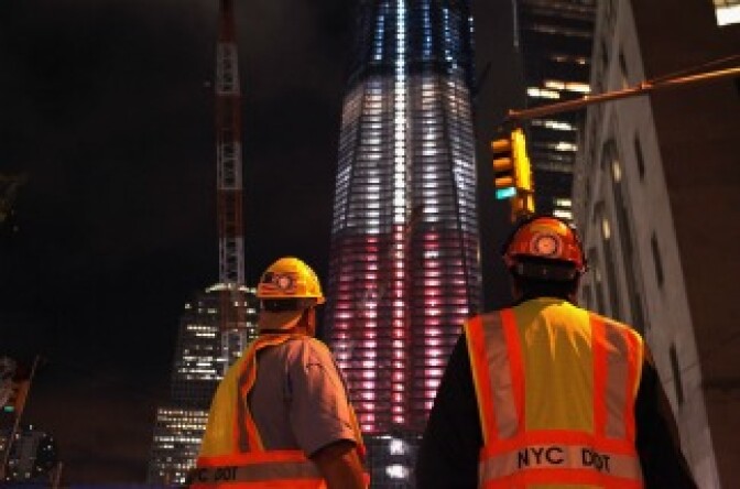 Construction workers look up at the Freedom Tower at the World Trade Center site which is lit in red, white and blue on September 8, 2011 in New York City.
