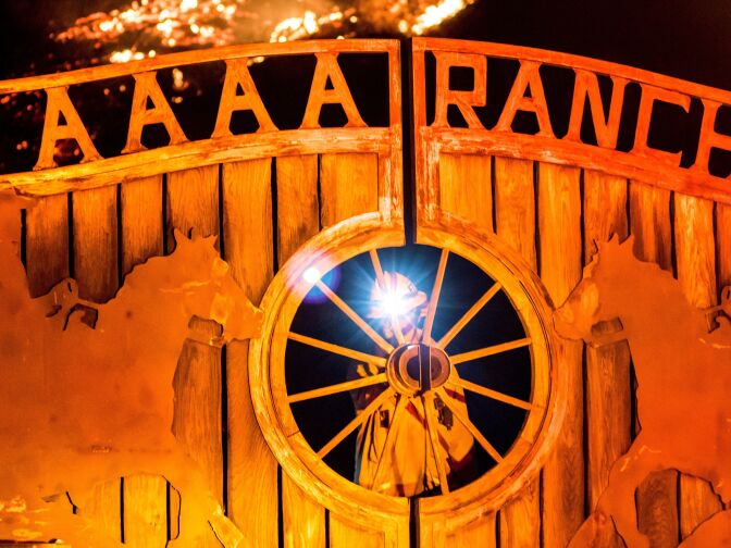 A firefighter opens a gate to investigate a house threatened by the Creek Fire as it burns along a hillside near homes in the Shadow Hills neighborhood of Los Angeles, California, on December 5, 2017.