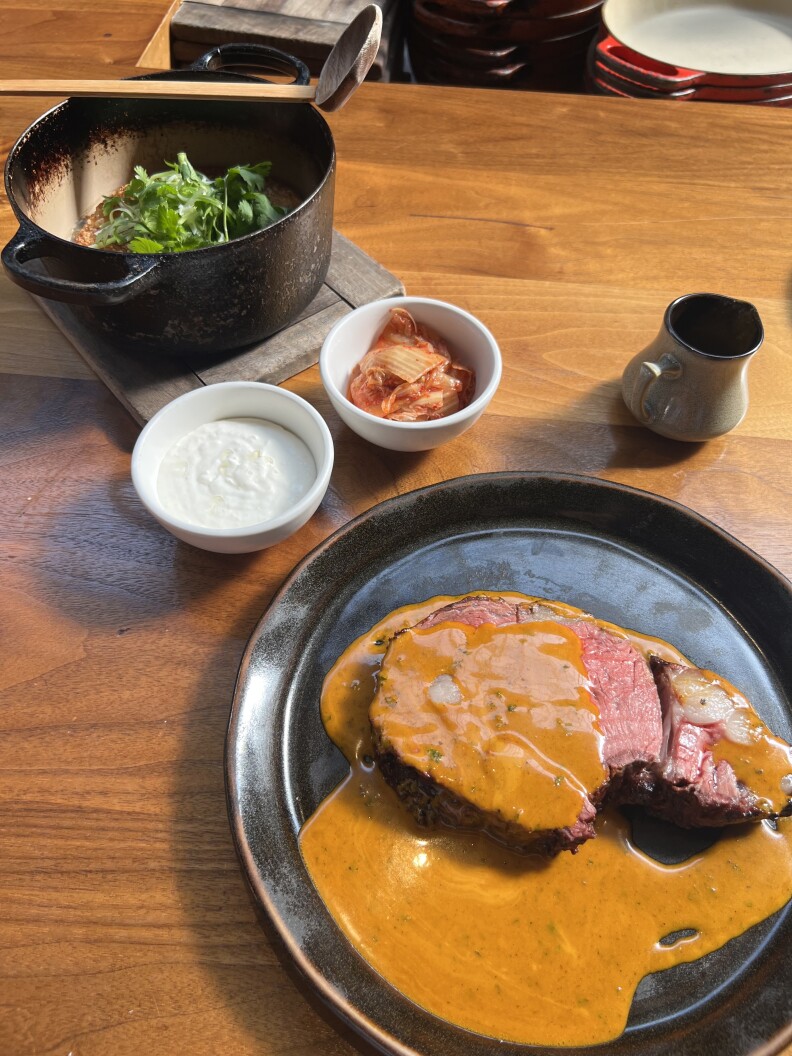 Waygu steak covered in a sauce is set out on a table with a side salad bowl nearby.