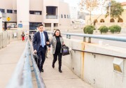 A young man in a suit and a middle-aged woman in a blazer walk up a ramp, both wearing expressions of tearful joy. 
