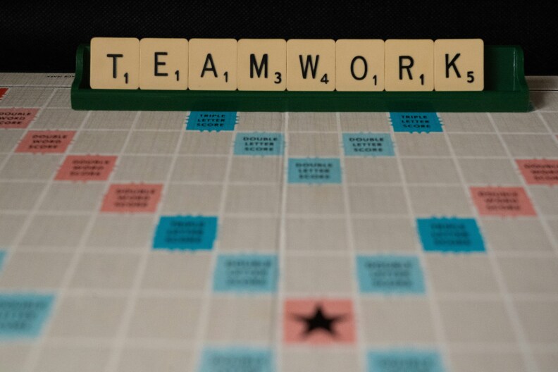 An empty scrabble game board. At the end of the board, a player's collection of letters spells "Teamwork," waiting to be played.