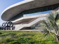 A building made of concrete and glass. Grass and palm trees are in front of the building.