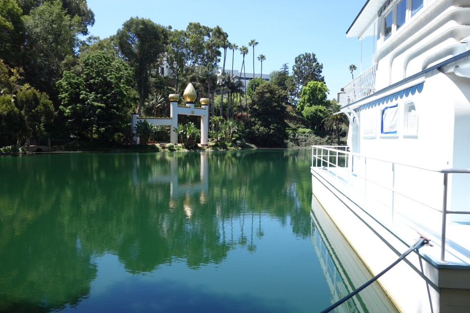 A white boat is visible on the right side of the picture, floating on a green-blue body of water. A golden and white shrine is visible across the body of water.