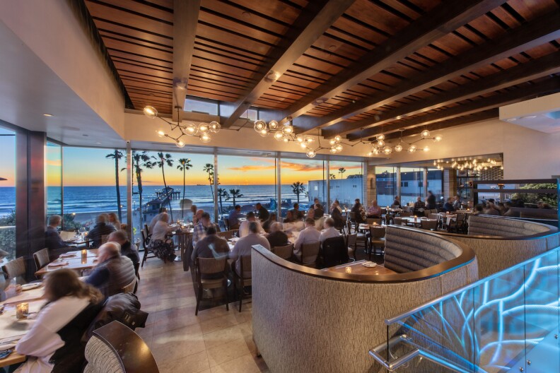 Patrons dine overlooking a colorful beachside sunset.