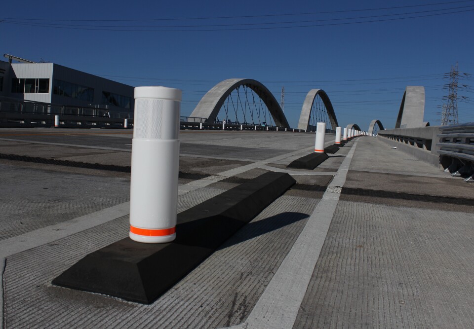 Rubber strips with plastic posts set on top span most of the length of a bridge to indicate a designated bicycle lane.