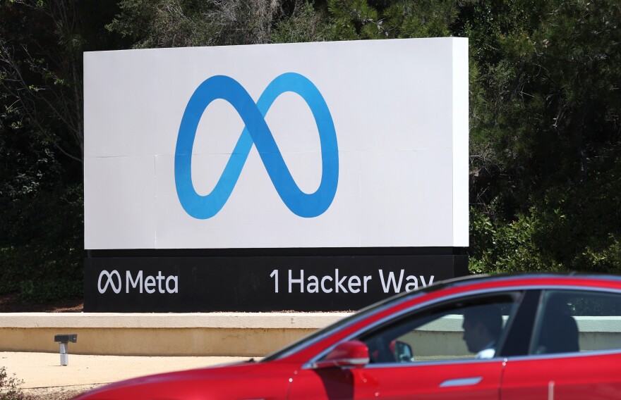 A red car passes a sign with the infinity-symbol-like Meta logo at 1 Hacker Way