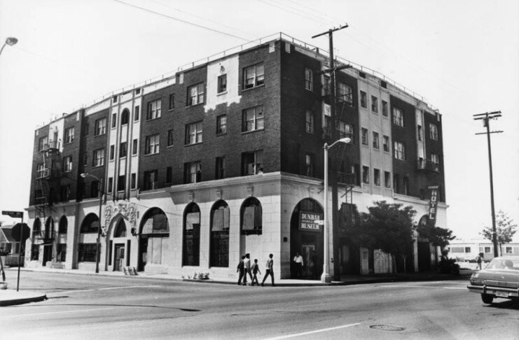 A black and white image of a four story corner building with a decorative first floor facade and tall rounded windows