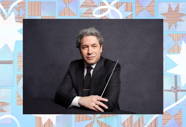 A musical conductor is posed for the camera, dressed in a dark suit and tie and holding his conductor's baton in his right hand.