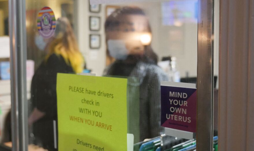 A sign reading "Mind Your Own Uterus" is taped on the check-in window at a women's health care clinic.